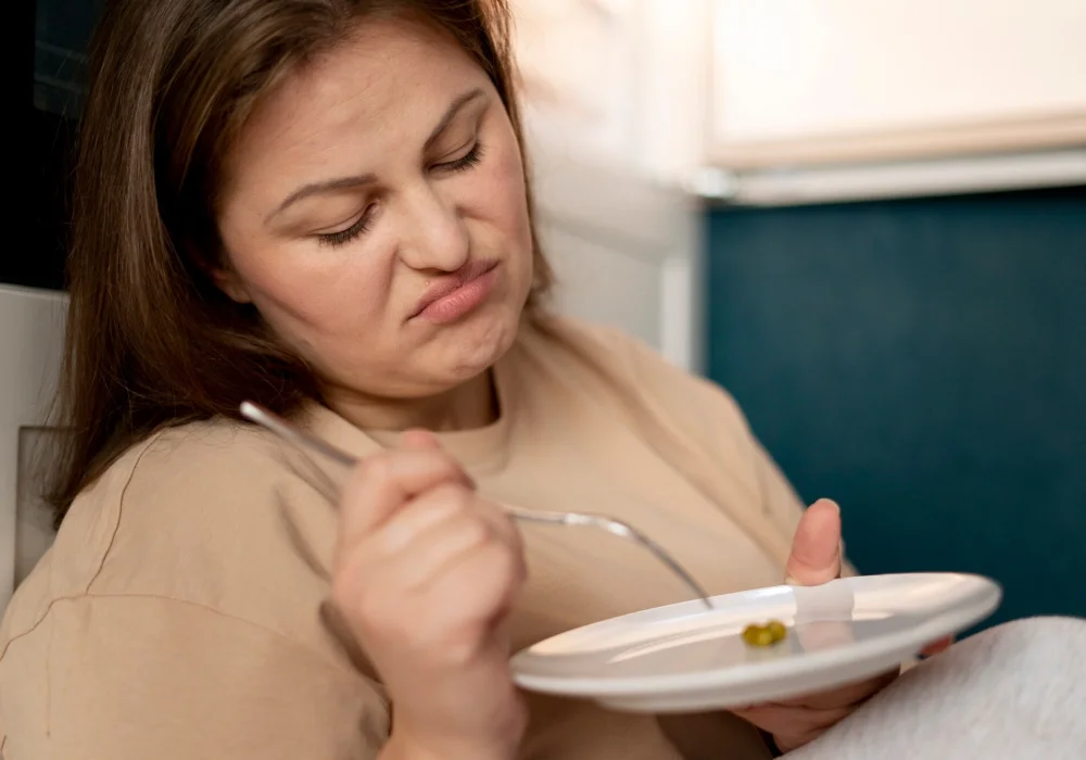 Kvinne ser motvillig på maten på tallerkenen – et illustrerende bilde brukt for å forsta-anorexia-nervosa-hos-voksne og deres forhold til matinntak.
