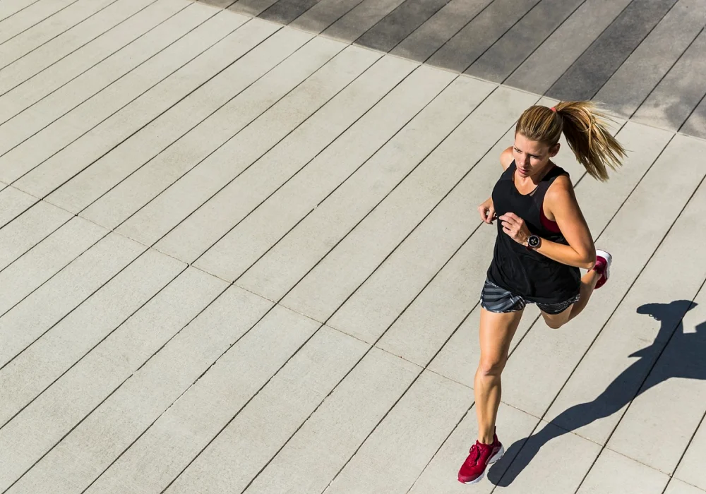 Kvinne som løper utendørs i sollys, iført sportsklær – et inspirerende bilde som illustrerer effektiv trening mot stress og bedre mental helse.